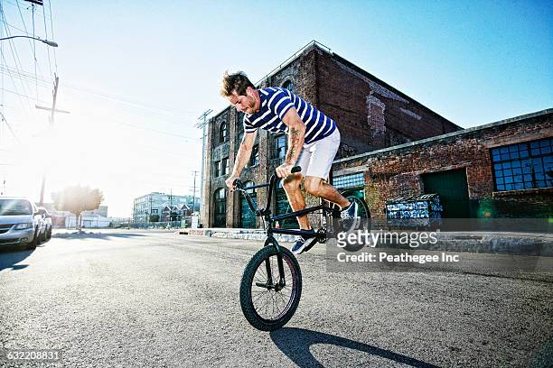 caucasian man riding bmx bike on street - bicycle stunt stock pictures, royalty-free photos & images