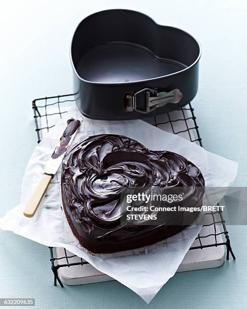 high angle view of heart shaped chocolate cake with chocolate ganache on cooling rack - cake tin stock pictures, royalty-free photos & images