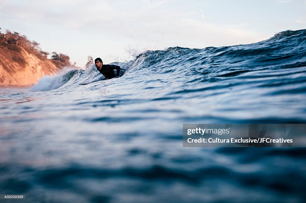 Surface level view of surfer lying on surfboard riding waves in ocean