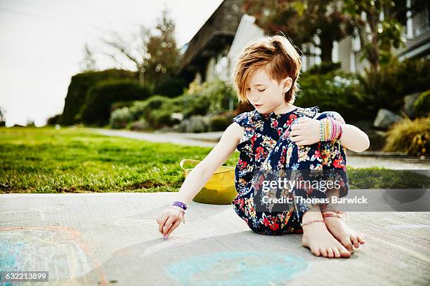 young girl sitting in driveway drawing with chalk - barefoot redhead ストックフォトと画像