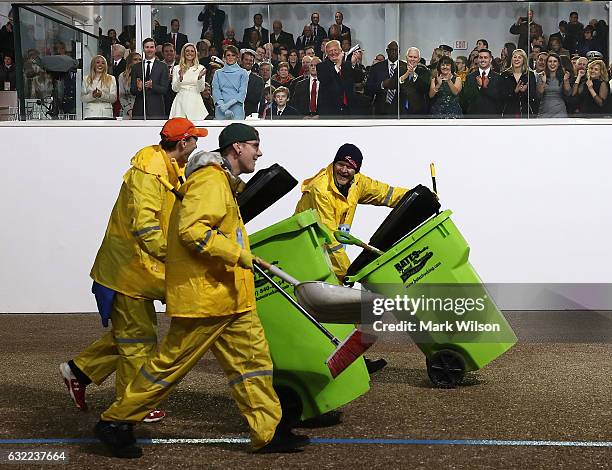 President Donald Trump watches as three men follow a horse detail to pick up any fallen debris, during inaugural parade in front of the White House...