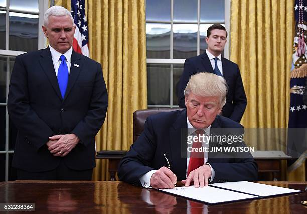 President Donald Trump signs an executive order as Vice President Mike Pence looks on at the White House in Washington, DC on January 20, 2017. / AFP...