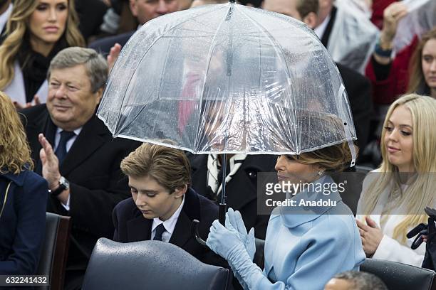 First Lady Melania Trump holds an umbrella over her and her son, Barron, while her husband, President Donald Trump, gives his Inaugural Address...