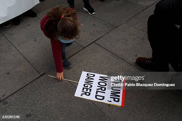 Girl picks up a placard reading 'Trump, world danger' during a demonstration in front of the US Embassy on January 21, 2017 in Madrid, Spain....