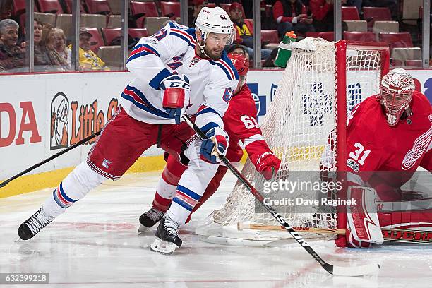 Rick Nash of the New York Rangers skates around the net with the puck in front of goaltender Jared Coreau of the Detroit Red Wings followed by Xavier...