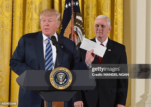 President Donald Trump holds the letter left for him by former US President Barack Obama, as Vice President Mike Pence watches, before the swearing...