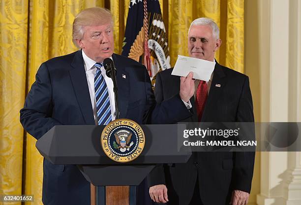 President Donald Trump holds the letter left for him by former US President Barack Obama, as Vice President Mike Pence watches, before the swearing...