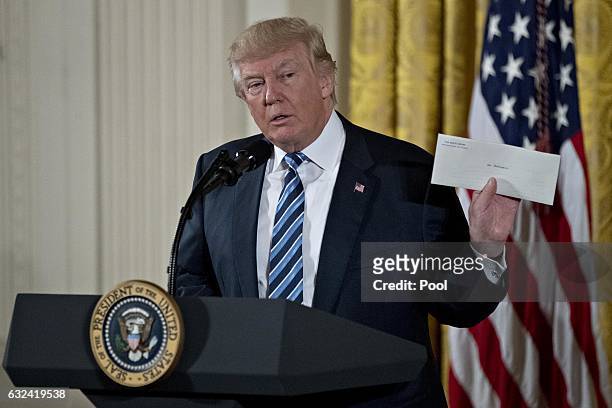 President Donald Trump holds up an envelope that was left for him in the Oval Office by former President Barack Obama during a swearing in ceremony...
