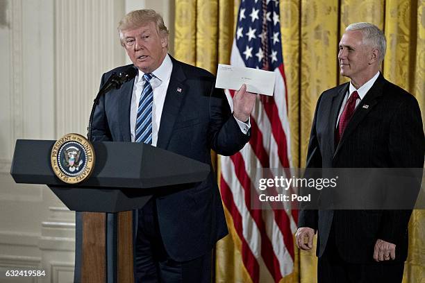 President Donald Trump holds up an envelope that was left for him in the Oval Office by former President Barack Obama next to U.S. Vice President...