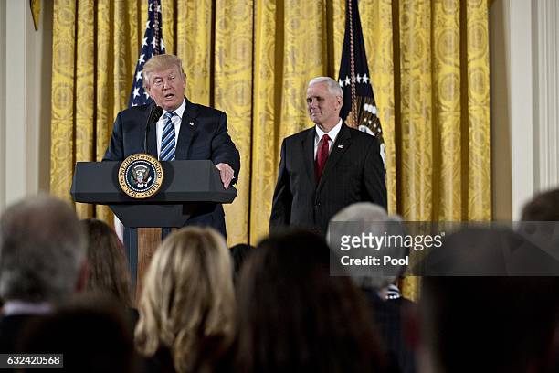 President Donald Trump speaks as U.S. Vice President Mike Pence listens during a swearing in ceremony of White House senior staff in the East Room of...