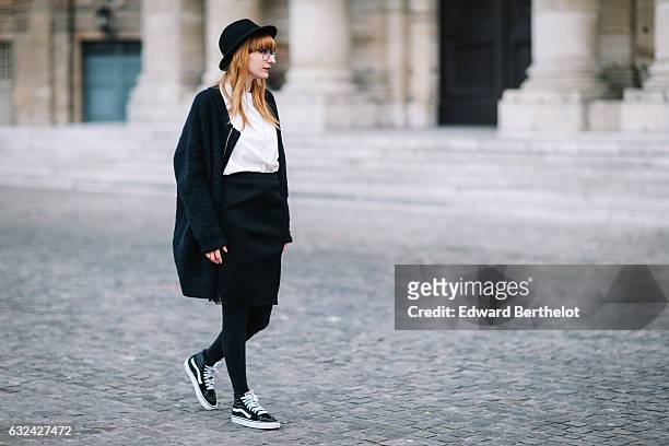Alyson Marion is wearing a black hat, a black cape, a white top, a black dress, black tights, and black shoes, during Paris Fashion Week Menswear...