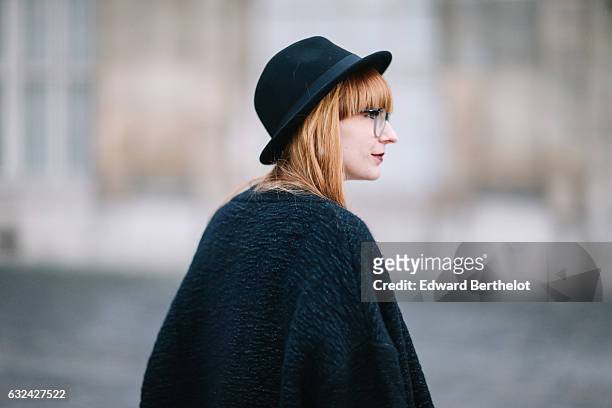 Alyson Marion is wearing a black hat, a black cape, a white top, a black dress, black tights, and black shoes, during Paris Fashion Week Menswear...