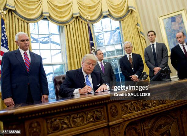 President Donald Trump signs an executive order alongside White House Chief of Staff Reince Priebus , US Vice President Mike Pence , National Trade...