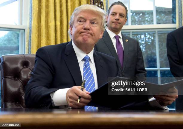 President Donald Trump signs an executive order as Chief of Staff Reince Priebus looks on in the Oval Office of the White House in Washington, DC,...