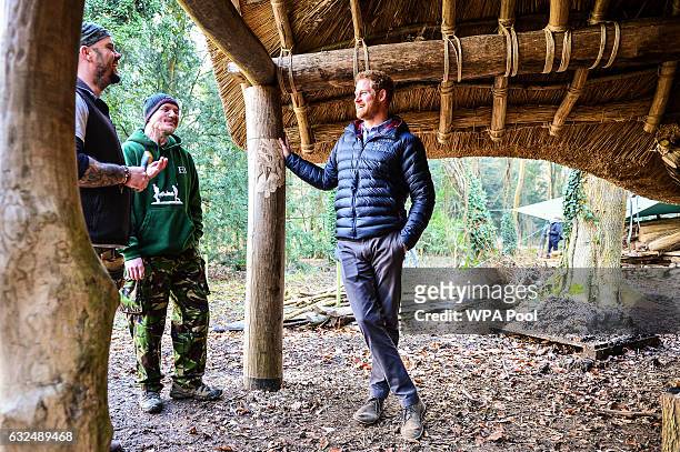 Prince Harry speaks with Mike Day and Eddie Beddoes underneath a mud, wood and thatched round house in the woodland area during a visit to a Help For...