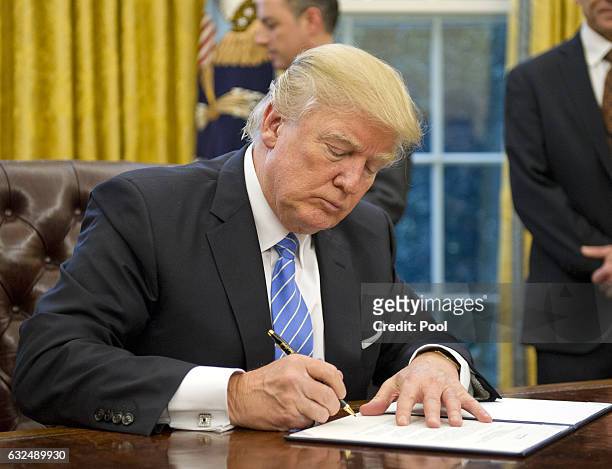 President Donald Trump signs the last of three Executive Orders in the Oval Office of the White House in Washington, DC on Monday, January 23, 2017....