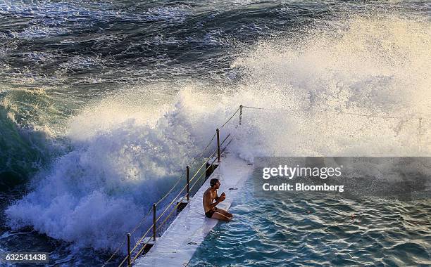 Man sits at the edge of a swimming pool at the Bondi Icebergs Swimming Club as a wave crashes against it at Bondi Beach in Sydney, Australia, on...