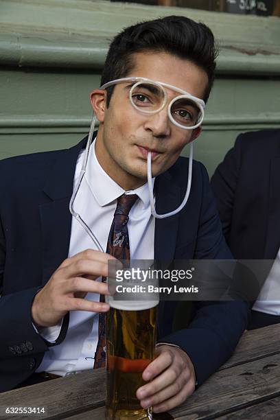 Young man drinking beer outside a London pub through a novelty straw in the shape of spectacles.
