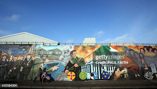 Woman with a pushchair walks past murals on the Falls road in west Belfast on January 23, 2017. Northern Ireland is facing its political turmoil with...
