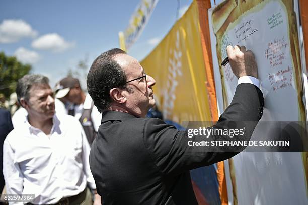 French President Francois Hollande writes a message during a visit to a FARC rebel disarmament zone next to Colombian President Juan Manuel Santos in...