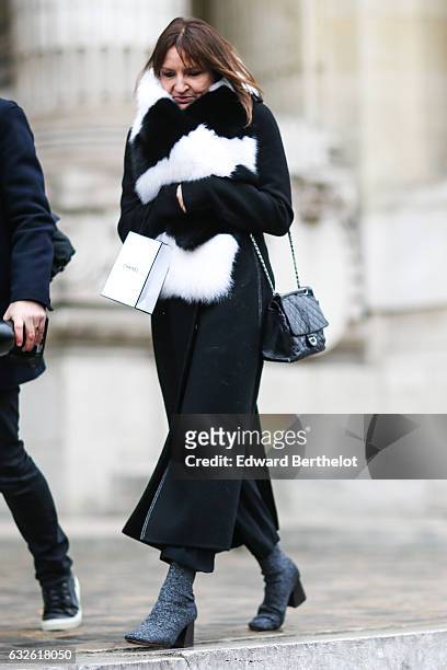 Guest wears a black and white fur scarf, a black long coat, and a Chanel bag, outside the Chanel show, at the Grand Palais, during Paris Fashion Week...