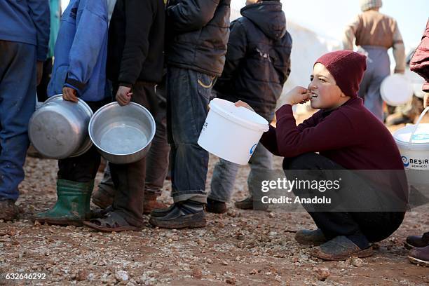 Boy holding a plastic bucket crouches as he waits in a queue to get meal at a tent city built up for the families coming from Aleppo, in northern...