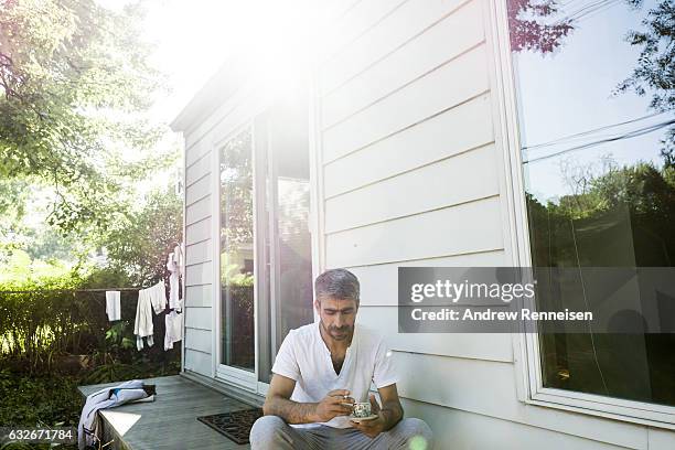 Muhammad Tanbal smokes a cigarette and sips coffee on the back porch of his new home on July 27, 2015 in Bloomfield hills, Michigan. He says he is...