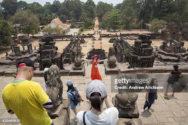 Woman in a red dress and bright pink hat poses for a photograph over the ancient site of Preah Ko temple, Roluos, Svay Chek District, Banteay...