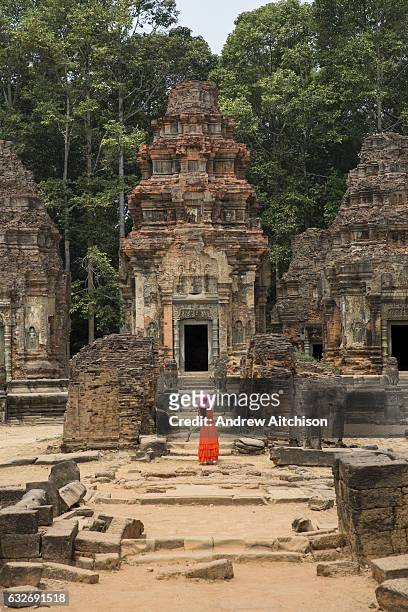 Woman in a red dress and bright pink hat stands in front of the central tower of the ancient Preah Ko temple, Roluos, Svay Chek District, Banteay...