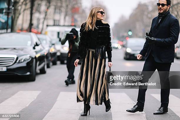 Olivia Palermo wears black sunglasses, a black fur coat, a striped dress, and black heels, outside the Elie Saab show, during Paris Fashion Week...
