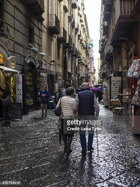 An elderly couple walk through Naples Centro Storico after the rain.
