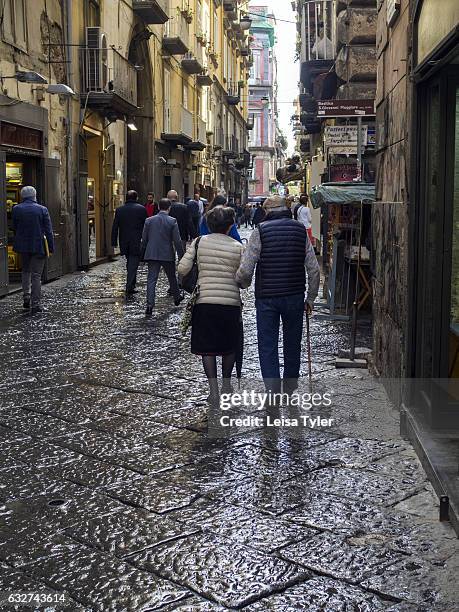 An elderly couple walk through Naples Centro Storico after the rain.