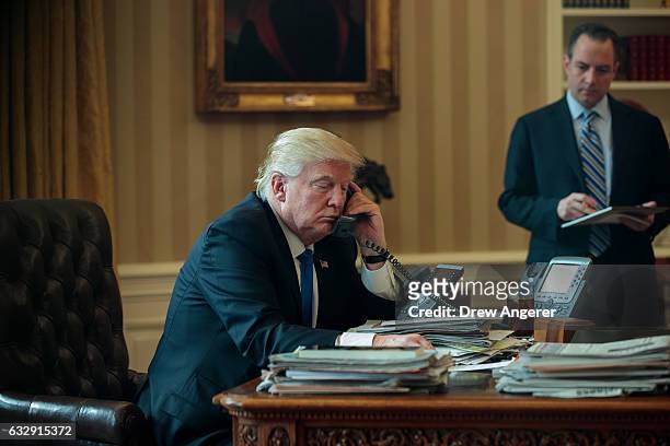 White House Chief of Staff Reince Priebus looks on as President Donald Trump speaks on the phone with Russian President Vladimir Putin in the Oval...