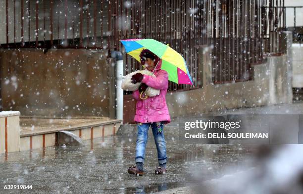 Syrian Kurdish girl walks with an umbrella during a snow storm in Qamishli, a Kurdish-majority city in Syria's northeastern Hasakeh province, on...