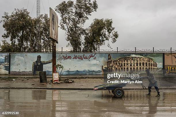 An Iraqi boy pushes a cart past an Islamic State proganada mural painted on a wall in east Mosul, Iraq, on January 28, 2017. The mural, featuring an...