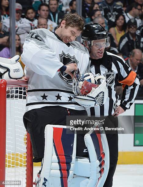Sergei Bobrovsky of the Columbus Blue Jackets adjusts his mask strap as NHL referee Kelly Sutherland looks on during the Metropolitan Division and...