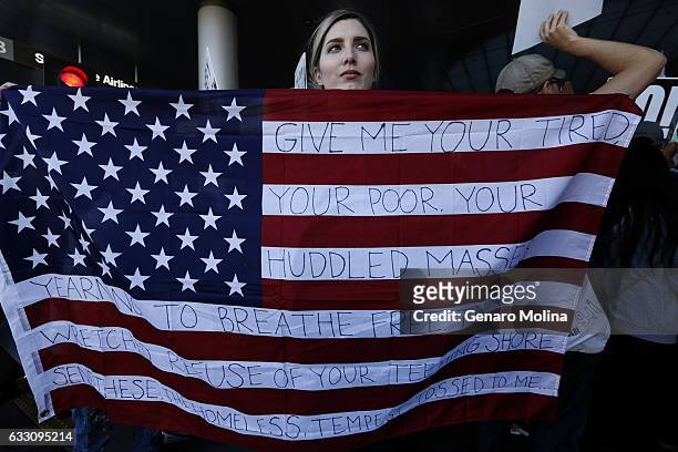 Chella, from Sherman Oaks, holds the U.S. Flag with words from the sonnet, "The New Colossus," by poet Emma Lazarus while joining people who continue...
