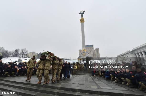 People kneel during a mourning ceremony on Independence Square in Kiev on February 1, 2017 as servicemen carry the coffins with the bodies of seven...