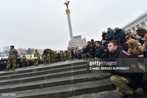 People kneel during a mourning ceremony on Independence Square in Kiev on February 1, 2017 as servicemen carry the coffins with the bodies of seven...