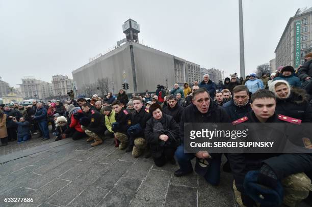 People kneel during a mourning ceremony on Independence Square in Kiev on February 1, 2017 as servicemen carry the coffins with the bodies of seven...