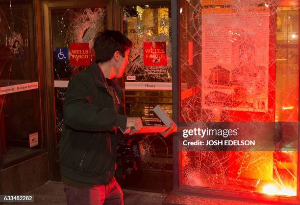 Man pulls a piece of metal out of a window as a flare burns inside a Wells Fargo Bank in Berkeley, California on February 2017. - A speech by...