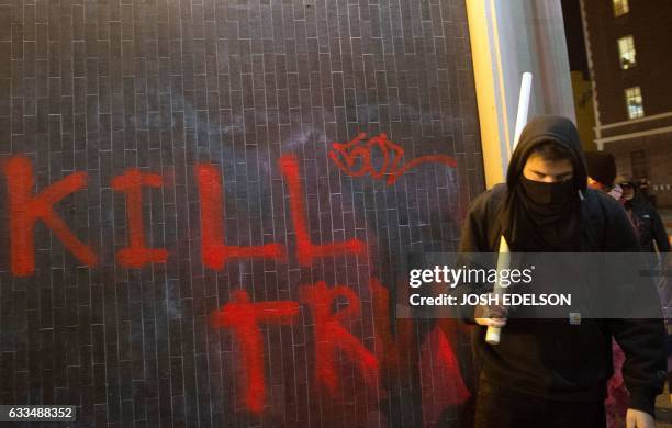 Protester walks with a pipe near graffiti in Berkeley, California on February 1, 2017. - Violent protests erupted on February 1 at the University of...