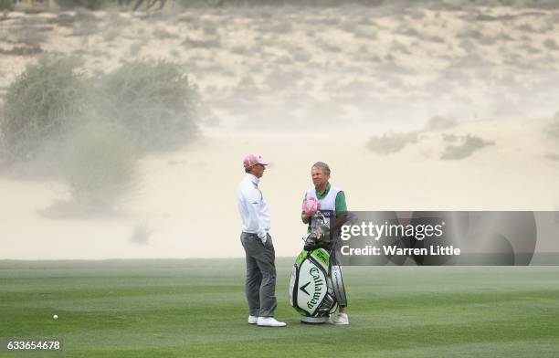 Callum Shinkwin of England stands with his caddie Dave McNeilly as winds blow sand across the course during the second round of the Omega Dubai...