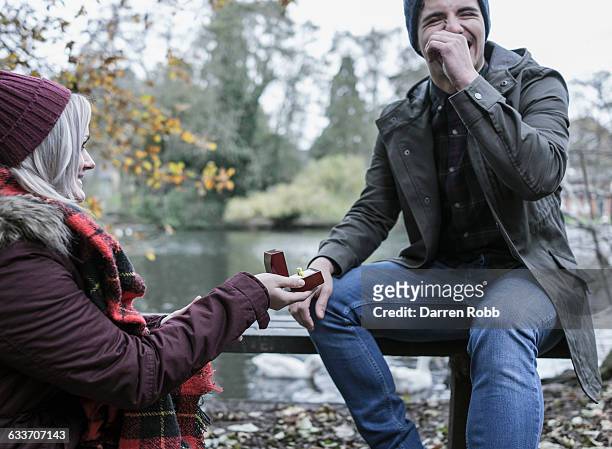 woman proposing to a man on a park bench - heiratsantrag stock-fotos und bilder