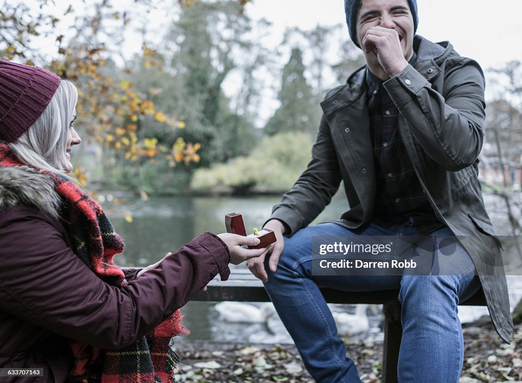 Woman proposing to a man on a park bench