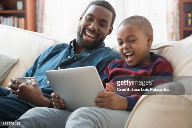 father and son using digital tablet on sofa - mood stream stock pictures, royalty-free photos & images