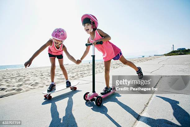 girls riding skateboard and scooter at beach - kinder kickboard stock-fotos und bilder