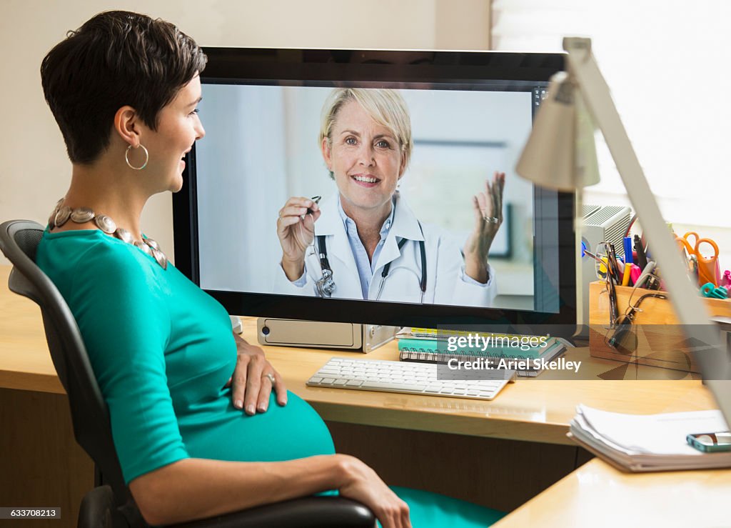 Pregnant mixed race businesswoman video chatting with doctor