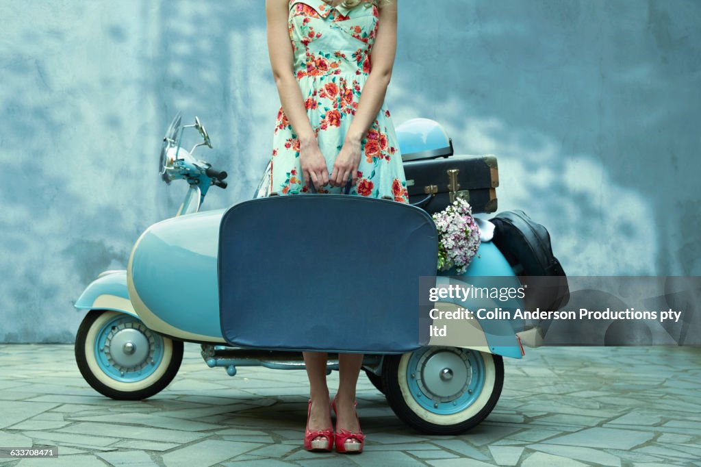 Pacific Islander woman holding suitcase near vintage scooter