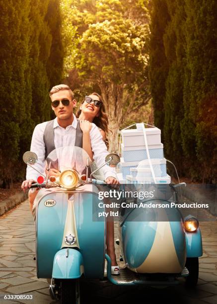 couple with gift boxes driving vintage scooter - wedding gift stockfoto's en -beelden